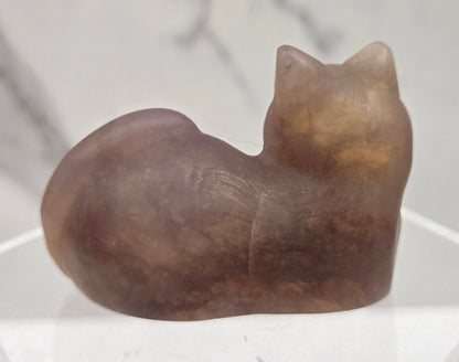 Pink crystal cat carving lying down an acrylic stand against a neutral background