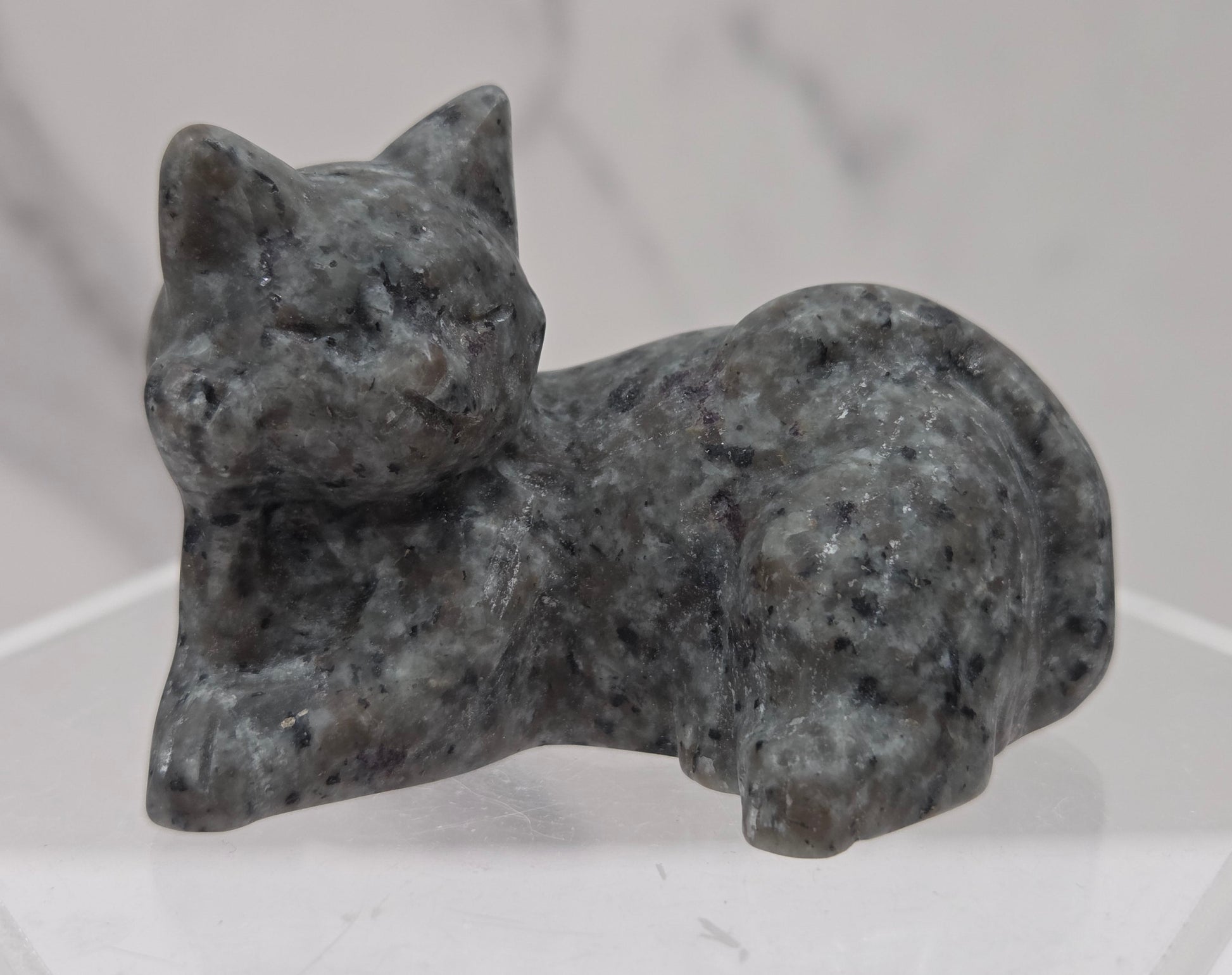 Yooperlite cat carving lying down an acrylic stand against a neutral background