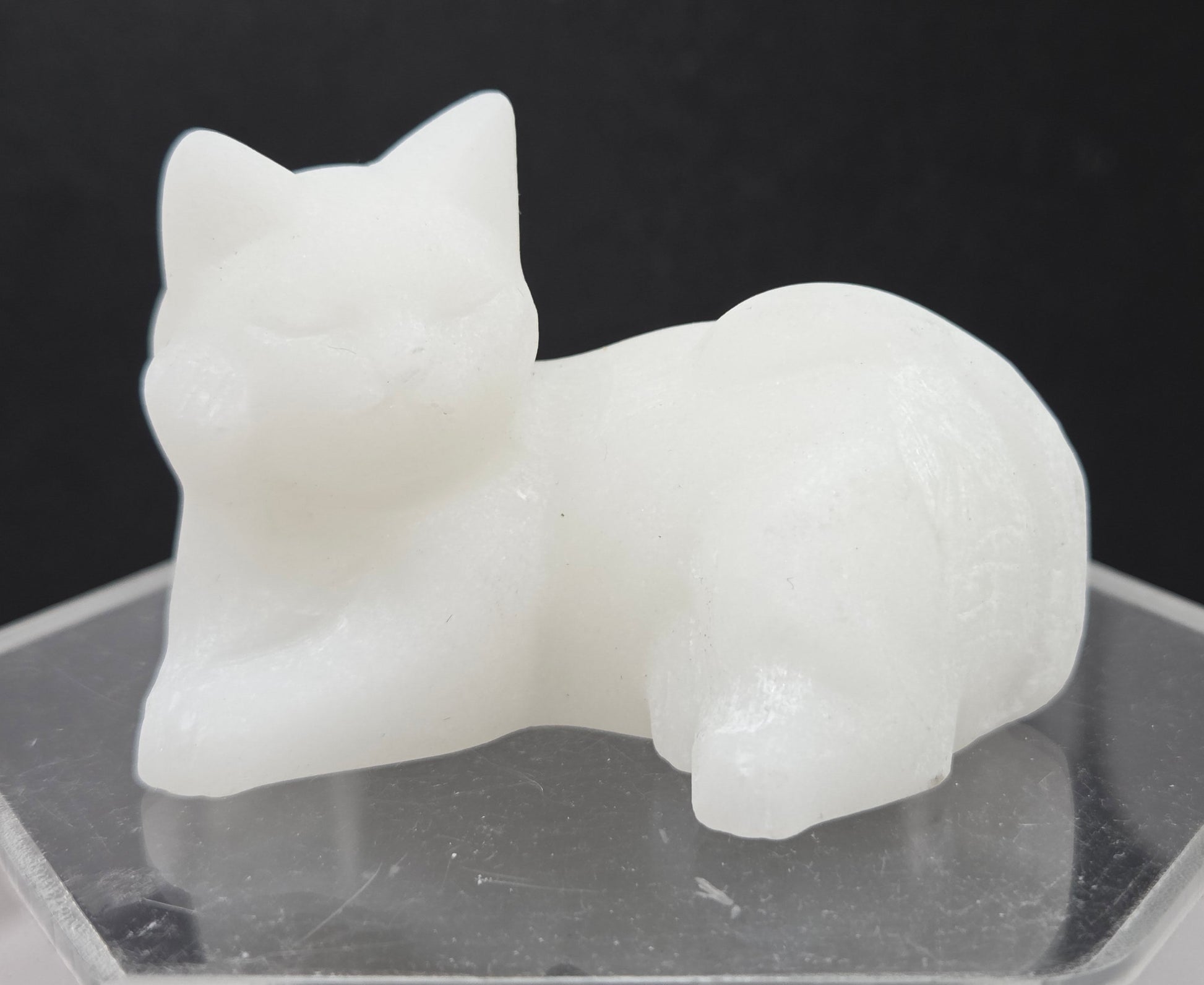 White Jade cat carving lying down an acrylic stand against a neutral background