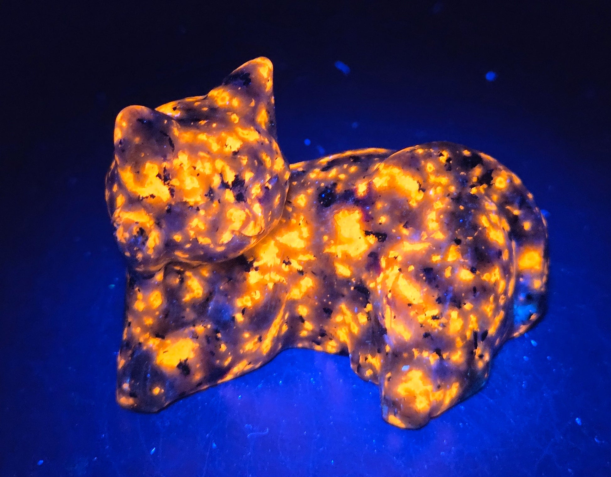 Yooperlite cat carving lying down against a neutral background under UV light
