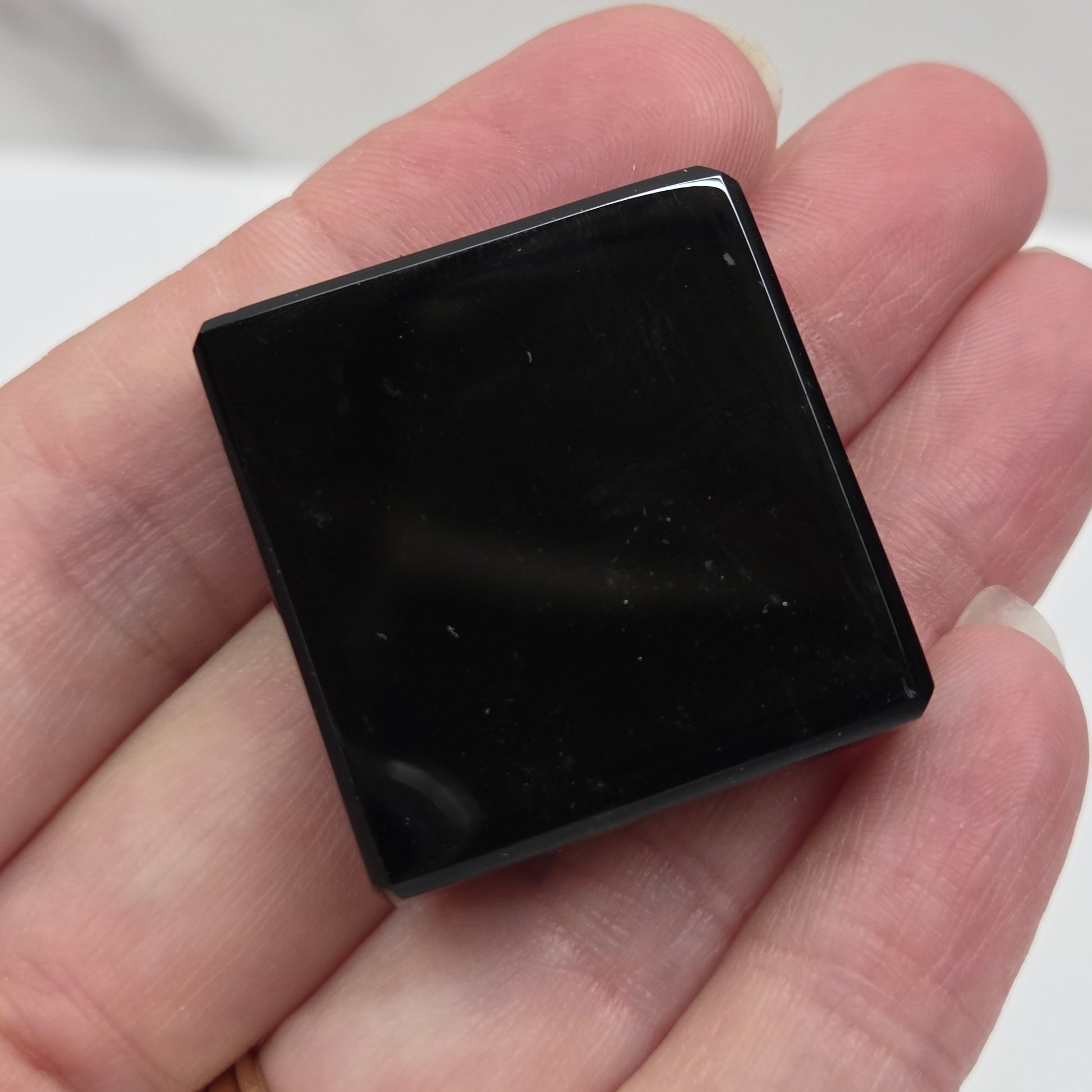 Small black square object held in a hand against a neutral background