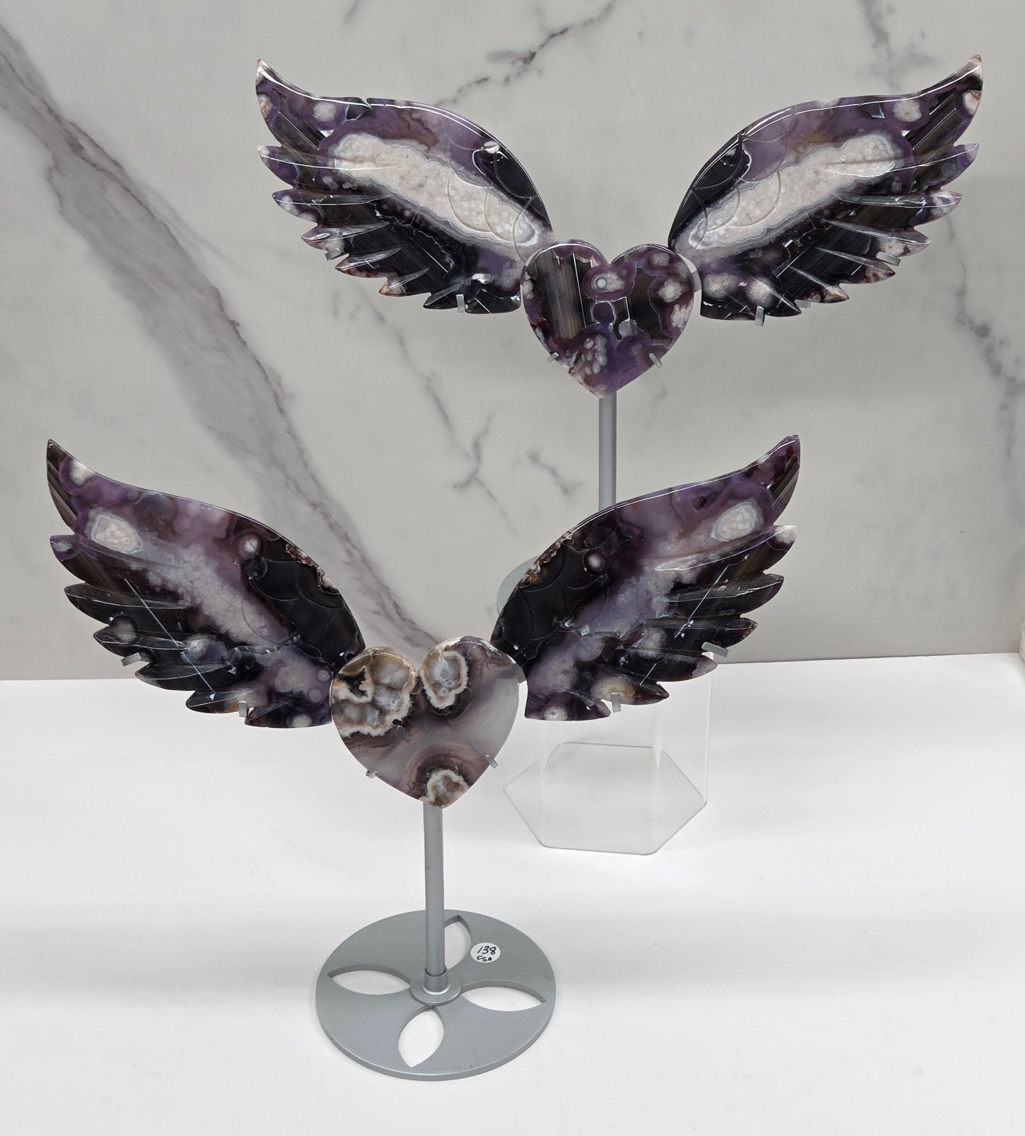 Black Flower Agate carved into wings and hearts on a silver stand against a white background.