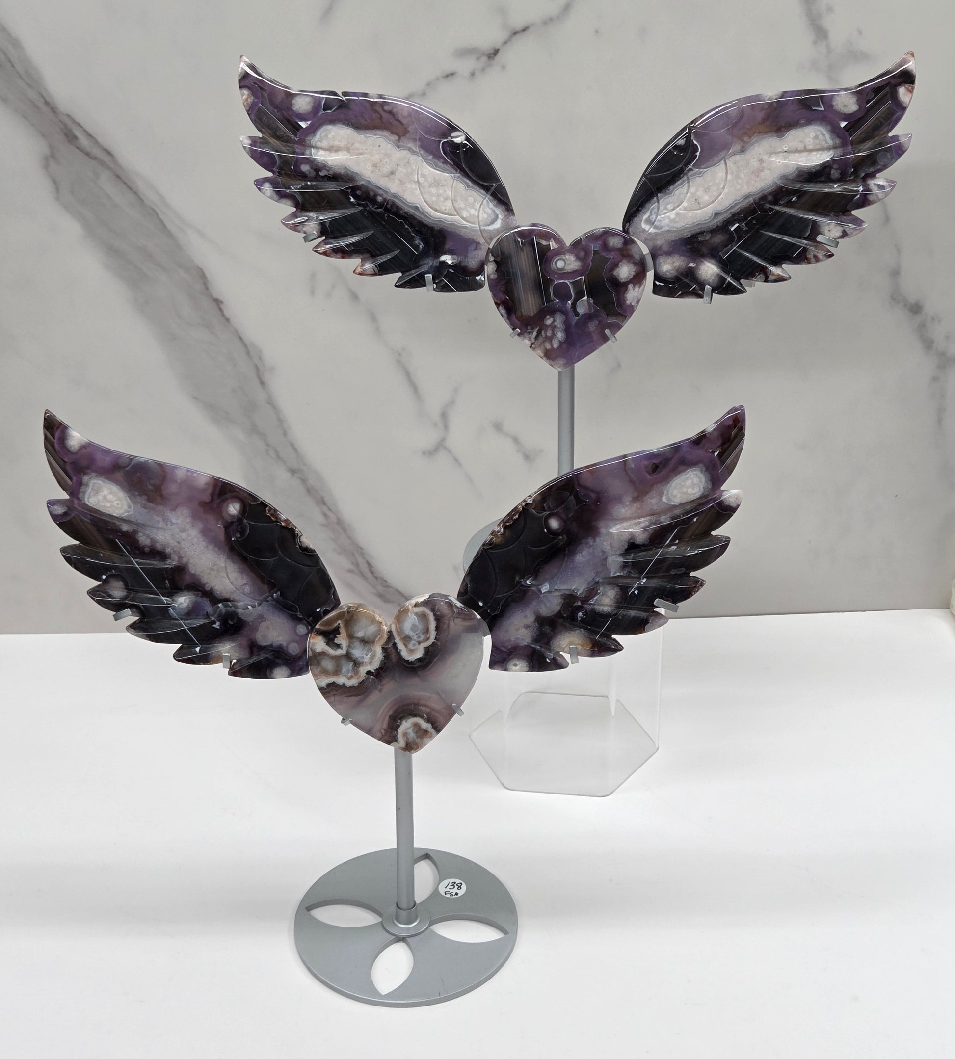 Black Flower Agate carved into wings and hearts on a silver stand against a white background.