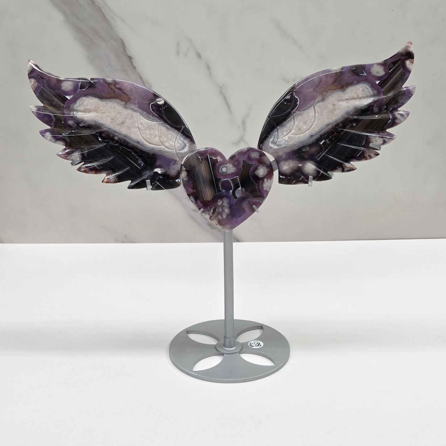 Black Flower Agate carved into wings and hearts on a silver stand against a white background.