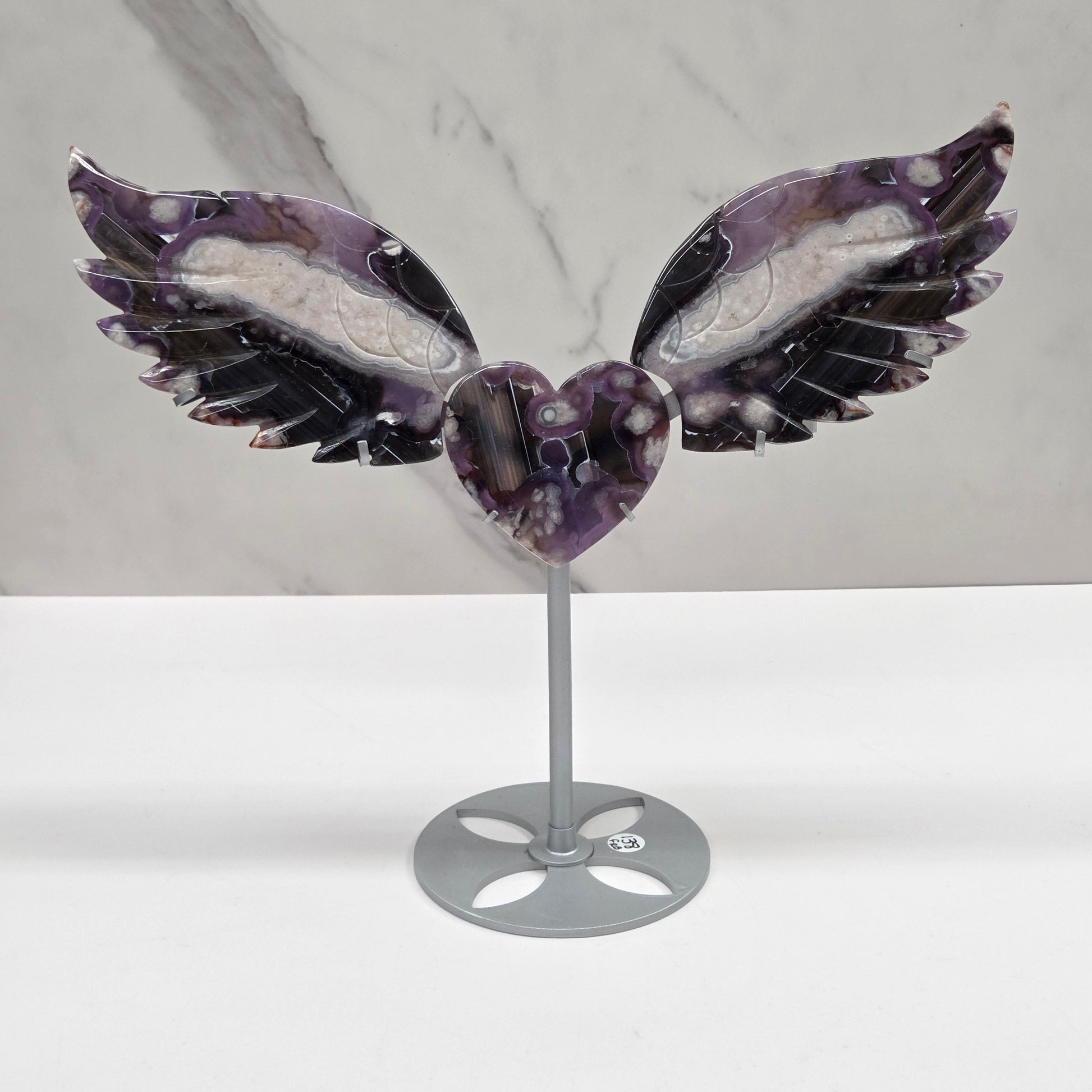 Black Flower Agate carved into wings and hearts on a silver stand against a white background.