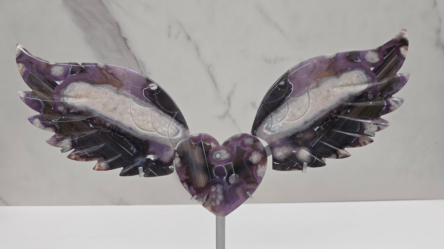 Black Flower Agate carved into wings and hearts on a silver stand against a white background.