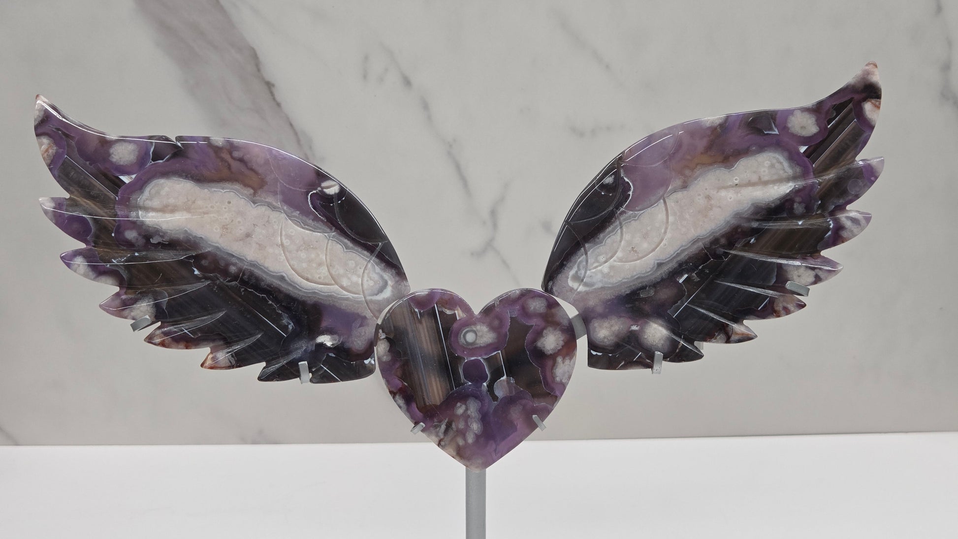 Black Flower Agate carved into wings and hearts on a silver stand against a white background.