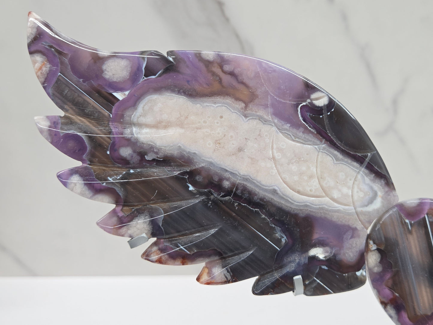 Black Flower Agate carved into wings and hearts on a silver stand against a white background.