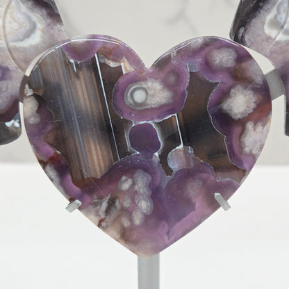 Black Flower Agate carved into wings and hearts on a silver stand against a white background.