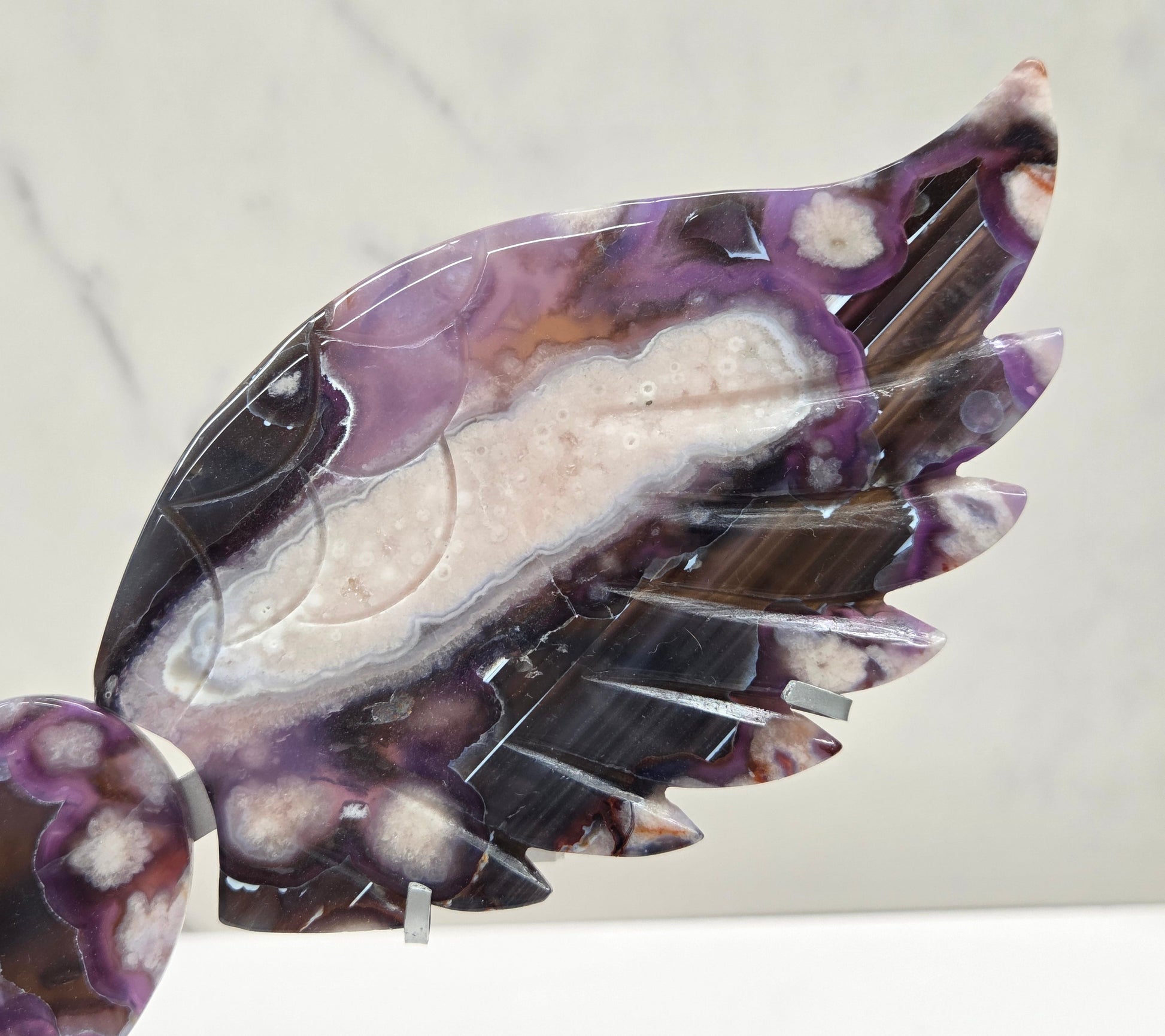 Black Flower Agate carved into wings and hearts on a silver stand against a white background.
