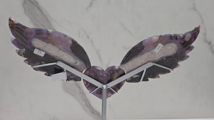 Black Flower Agate carved into wings and hearts on a silver stand against a white background.