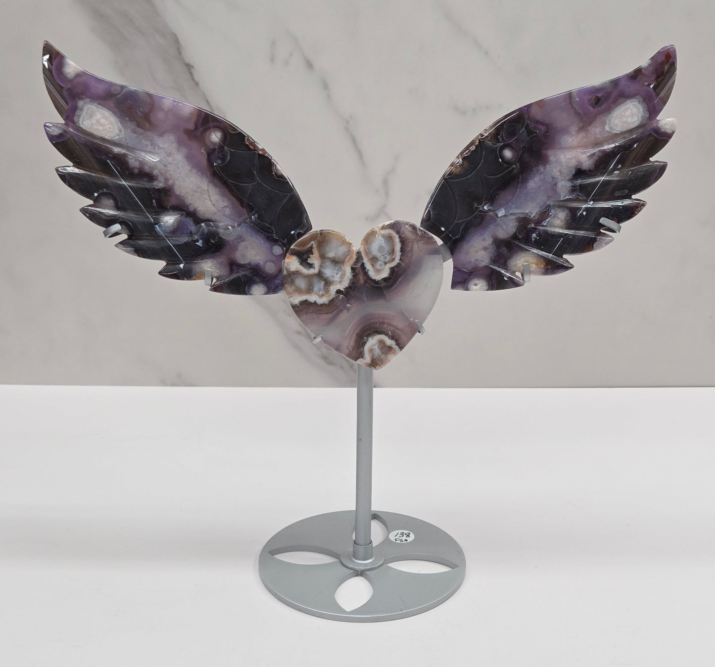 Black Flower Agate carved into wings and hearts on a silver stand against a white background.