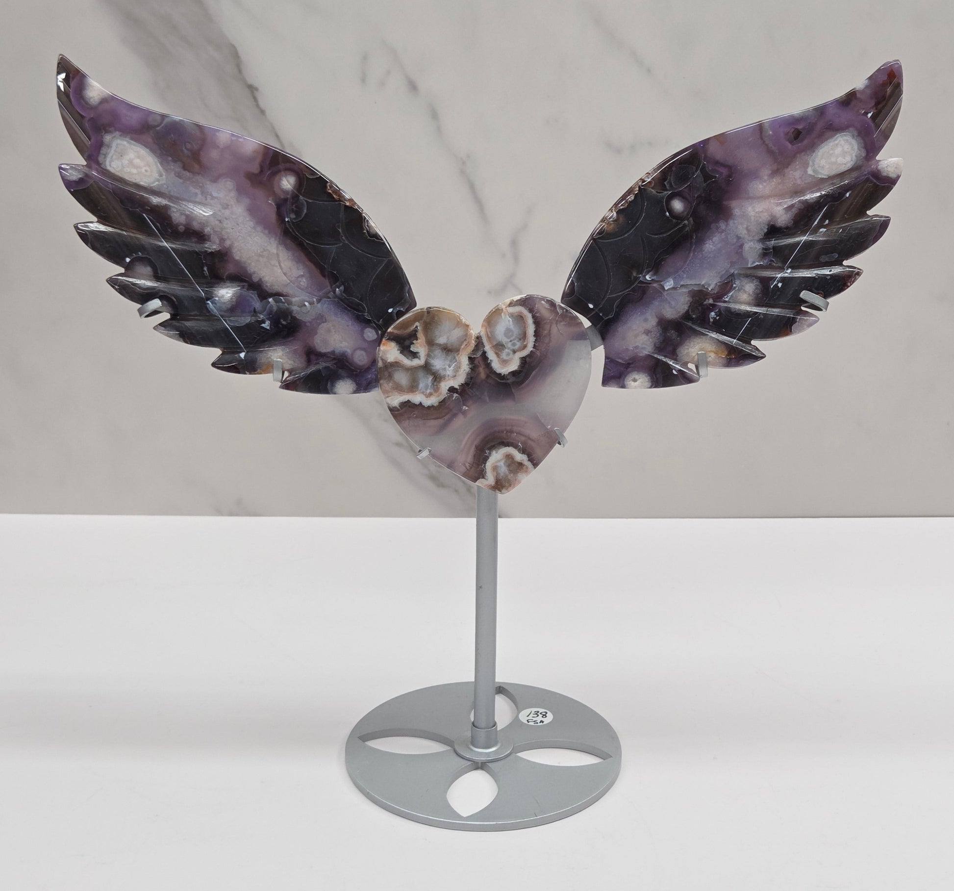 Black Flower Agate carved into wings and hearts on a silver stand against a white background.