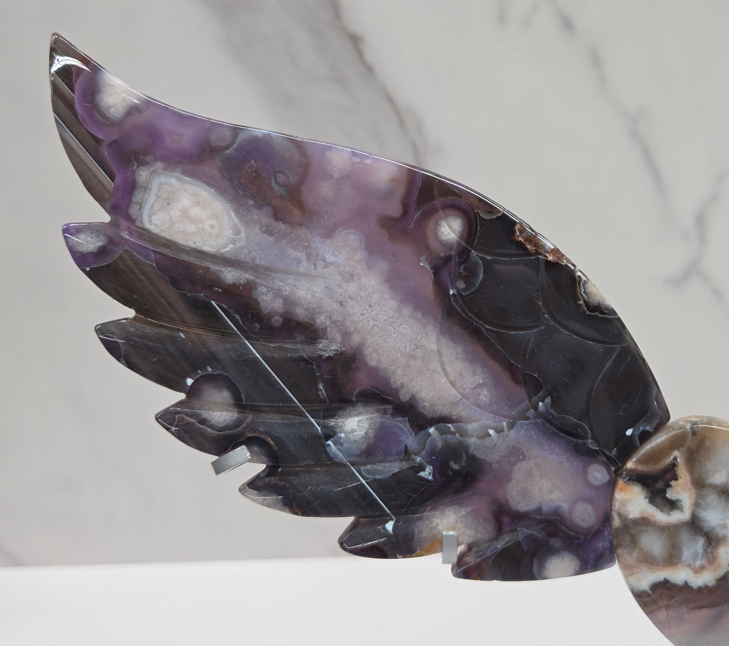 Black Flower Agate carved into wings and hearts on a silver stand against a white background.