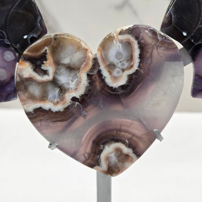 Black Flower Agate carved into wings and hearts on a silver stand against a white background.