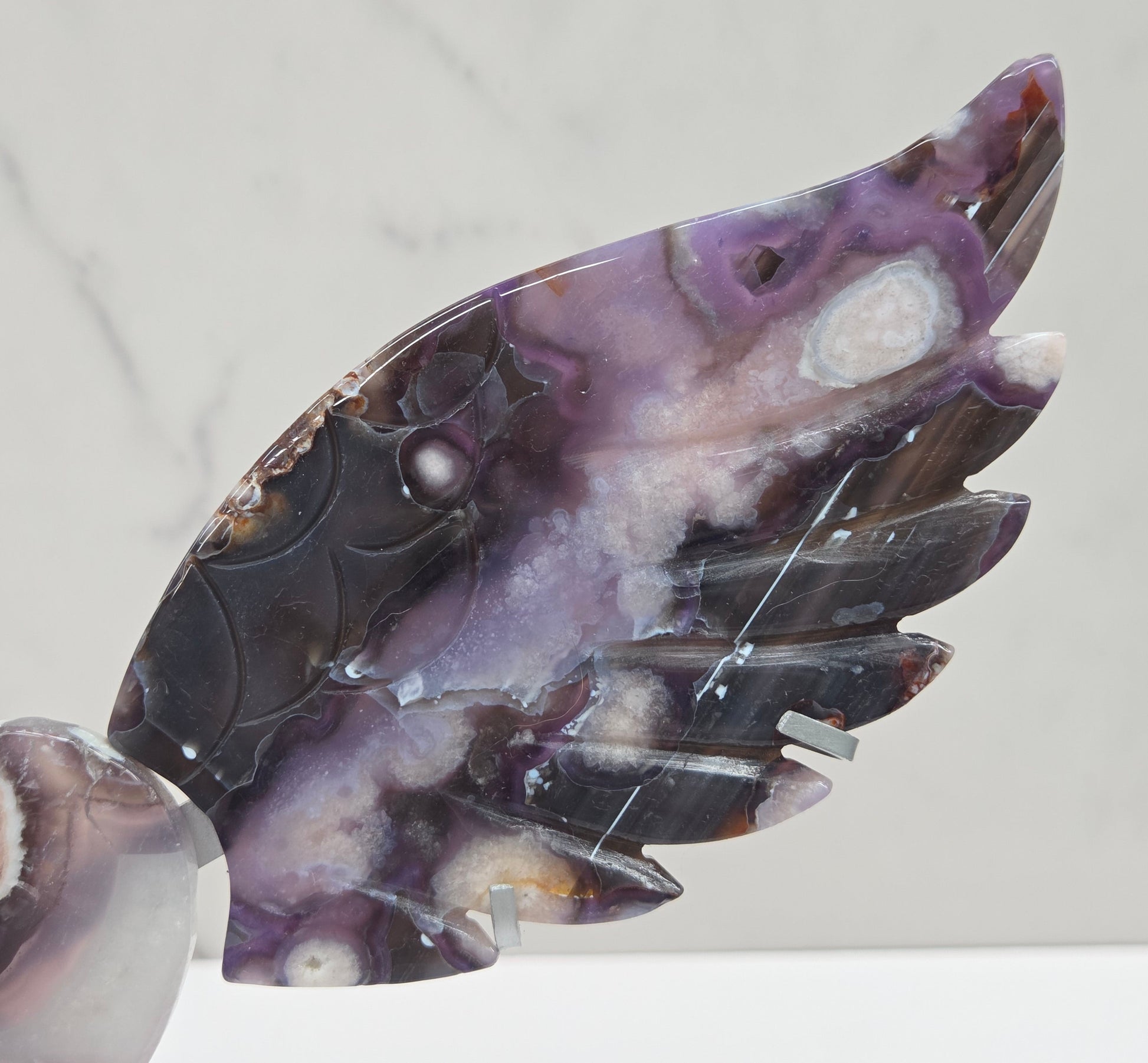 Black Flower Agate carved into wings and hearts on a silver stand against a white background.