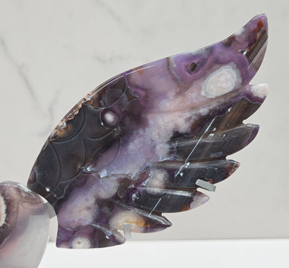 Black Flower Agate carved into wings and hearts on a silver stand against a white background.