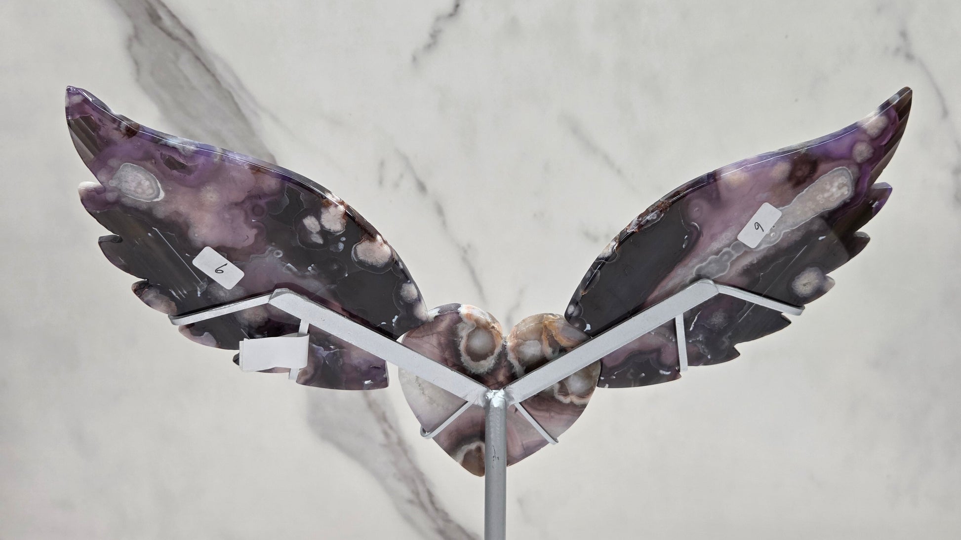 Black Flower Agate carved into wings and hearts on a silver stand against a white background.