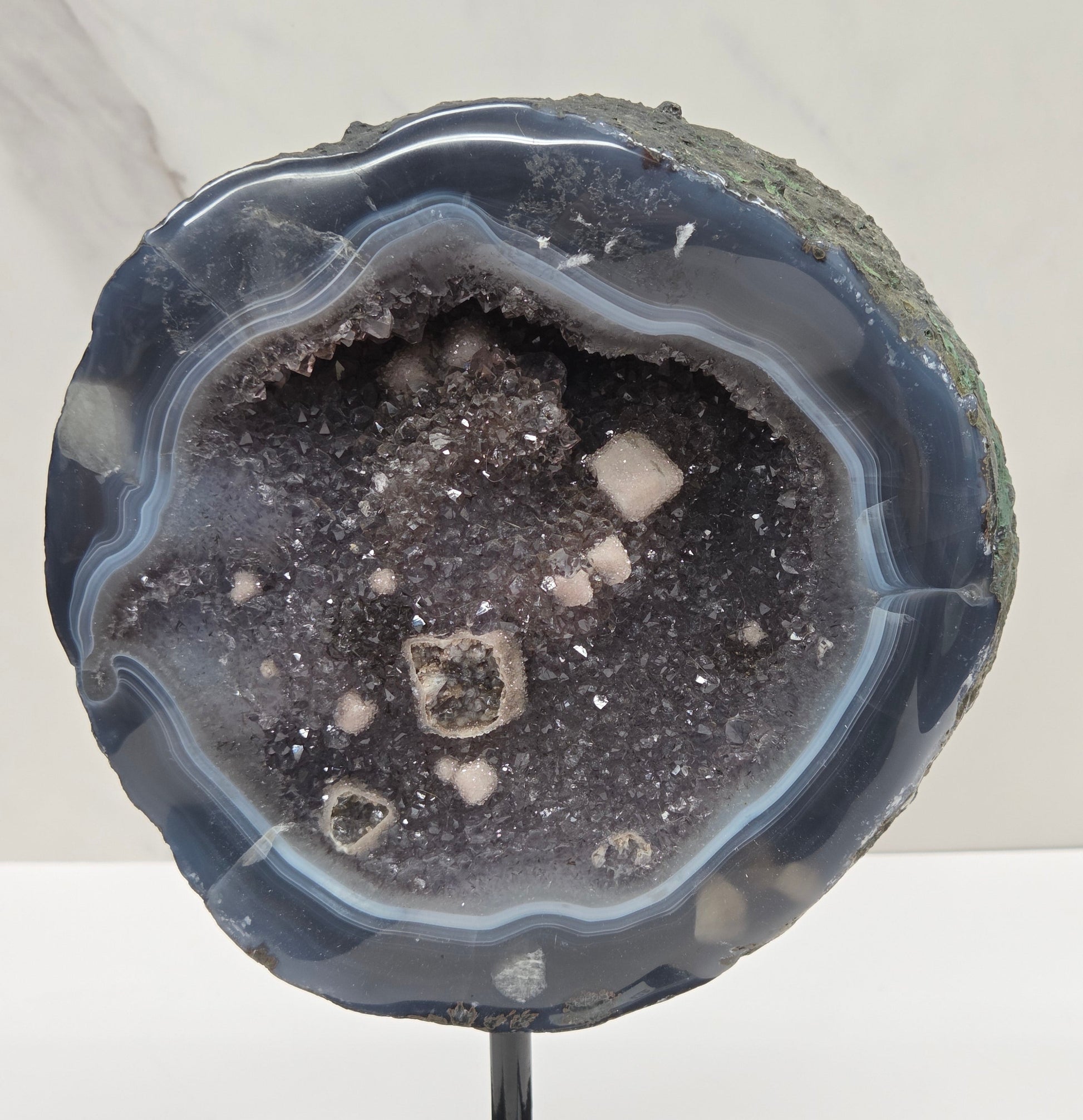 Amethyst and Agate round geode with white calcite inclusions on a black stand against a white background