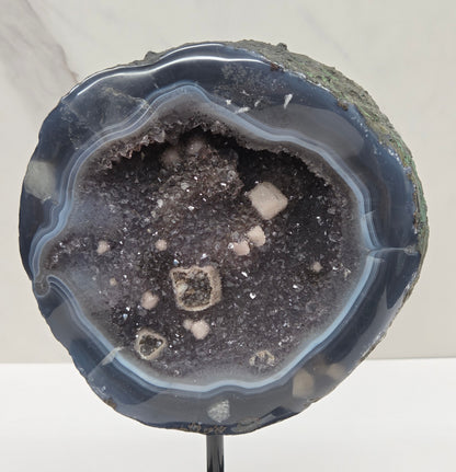 Amethyst and Agate round geode with white calcite inclusions on a black stand against a white background
