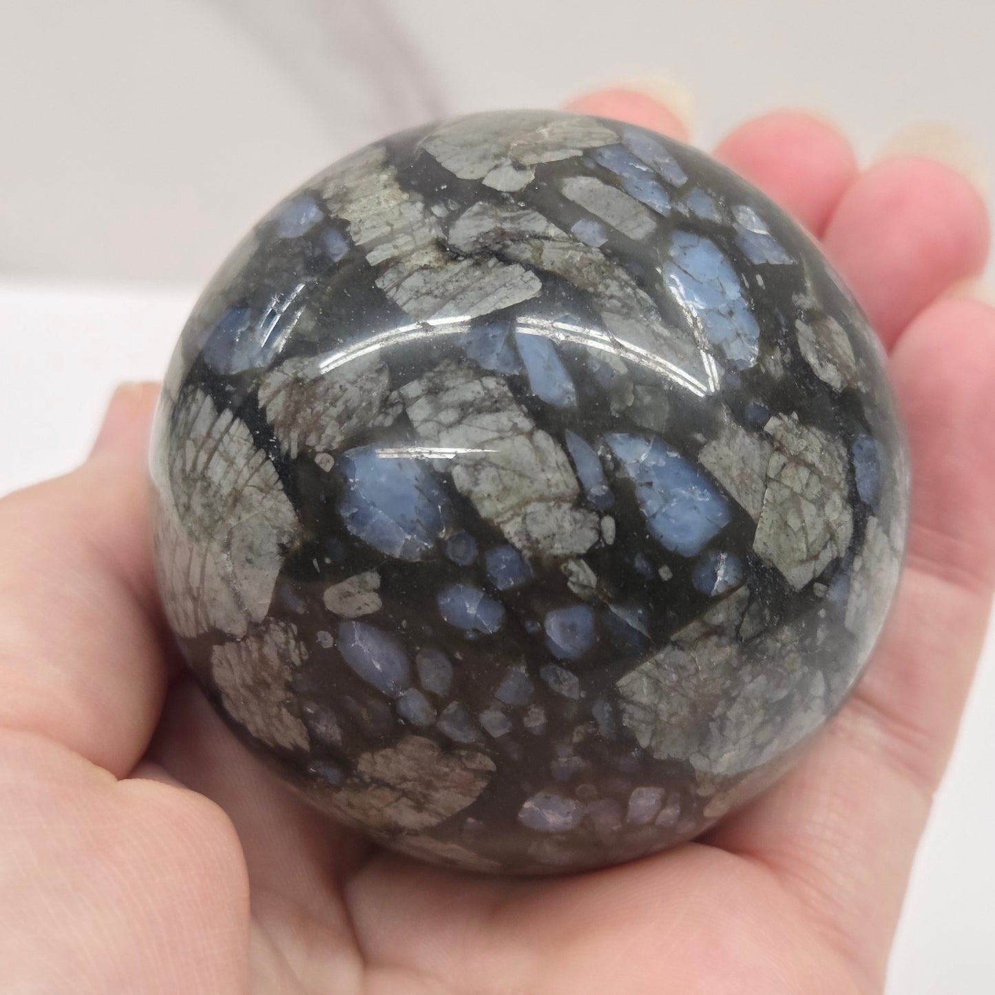 Blue grey and black sphere being held by a hand against a white background