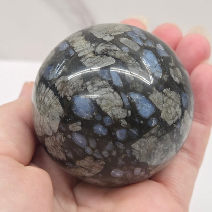 Blue grey and black sphere being held by a hand against a white background