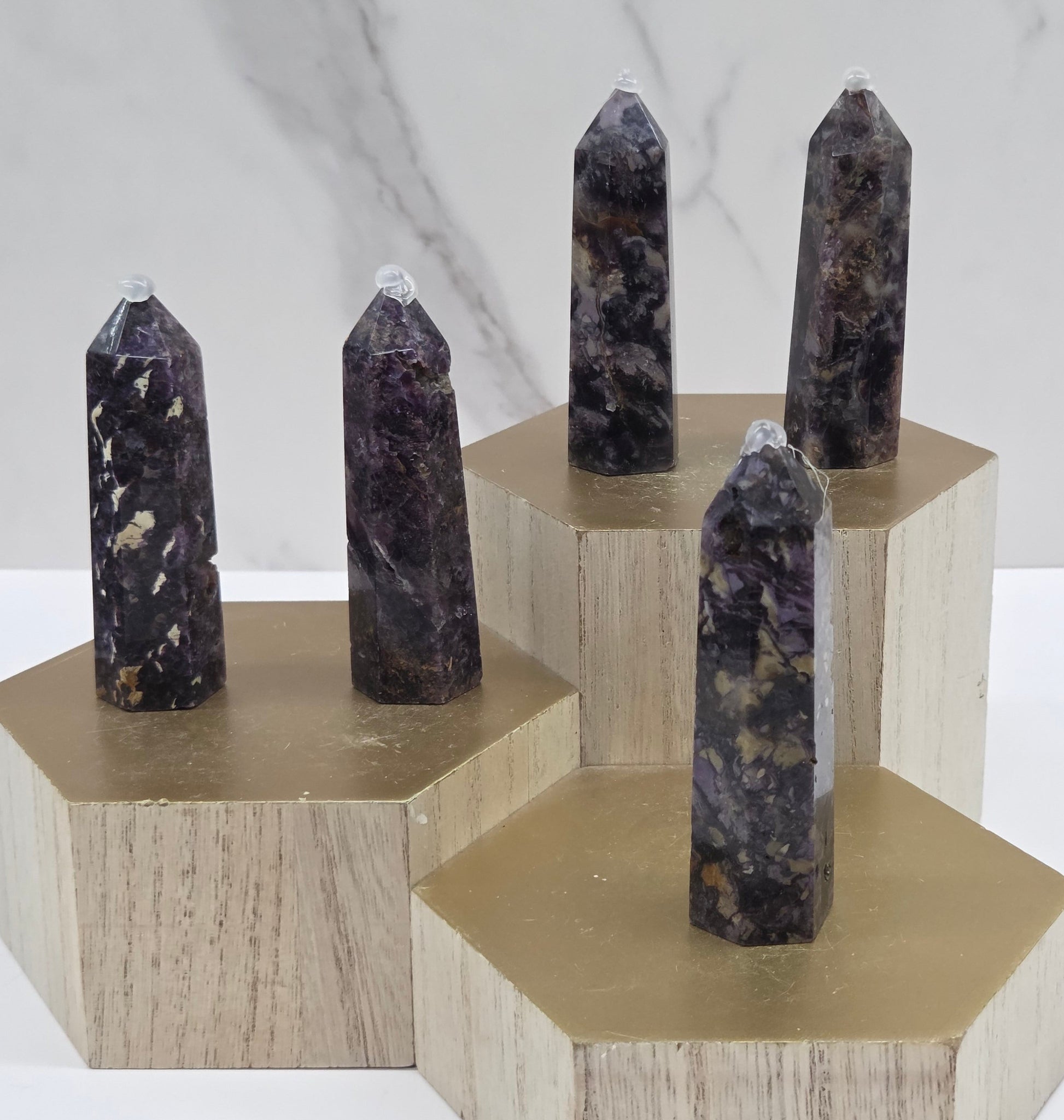 Brecciated Fluorite towers on a wooden stand against a white background