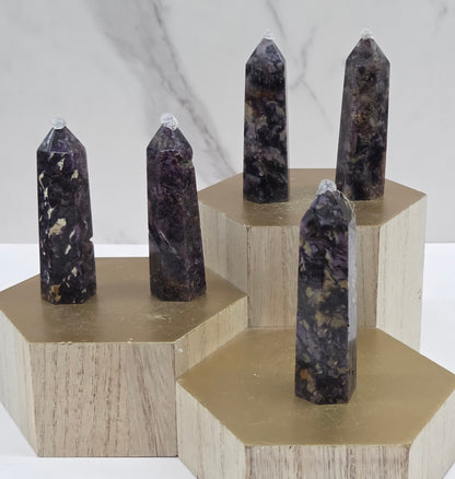 Brecciated Fluorite towers on a wooden stand against a white background
