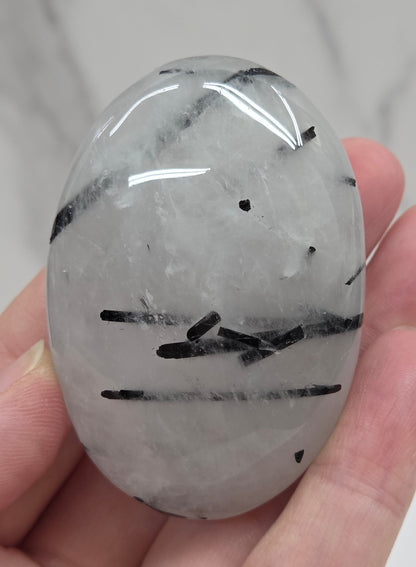 Palm shaped carving made of Quartz with Tourmaline inclusions being held in a hand on a white background