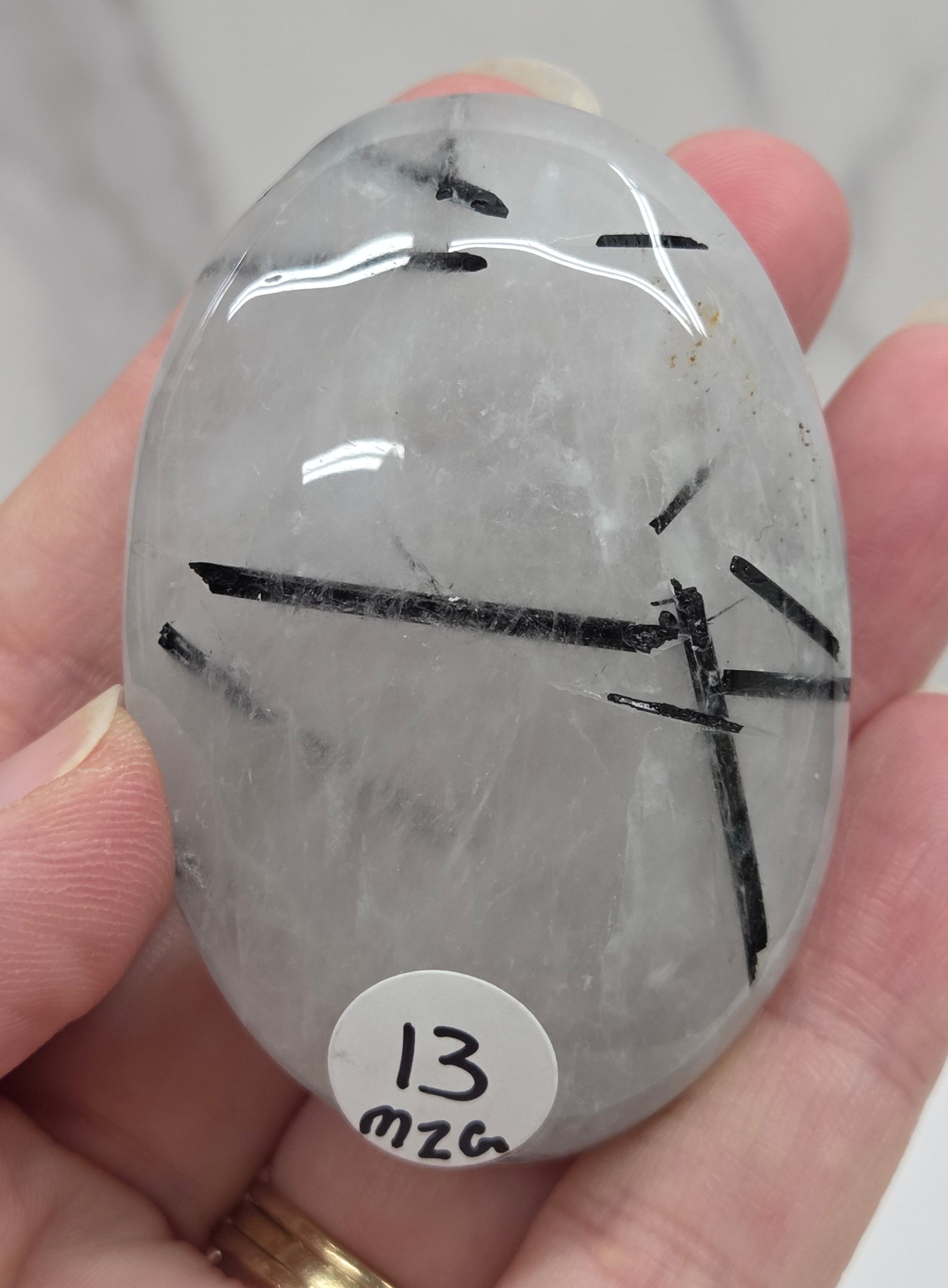 Palm shaped carving made of Quartz with Tourmaline inclusions being held in a hand on a white background