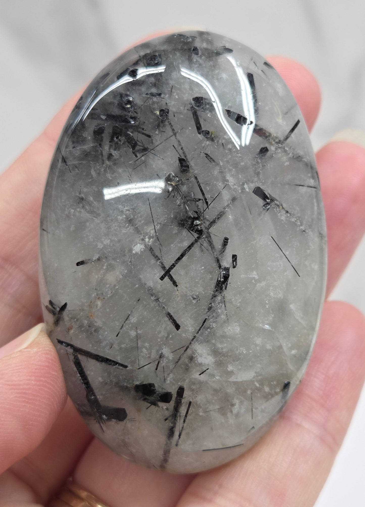 Palm shaped carving made of Quartz with Tourmaline inclusions being held in a hand on a white background