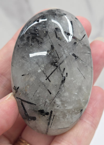 Palm shaped carving made of Quartz with Tourmaline inclusions being held in a hand on a white background