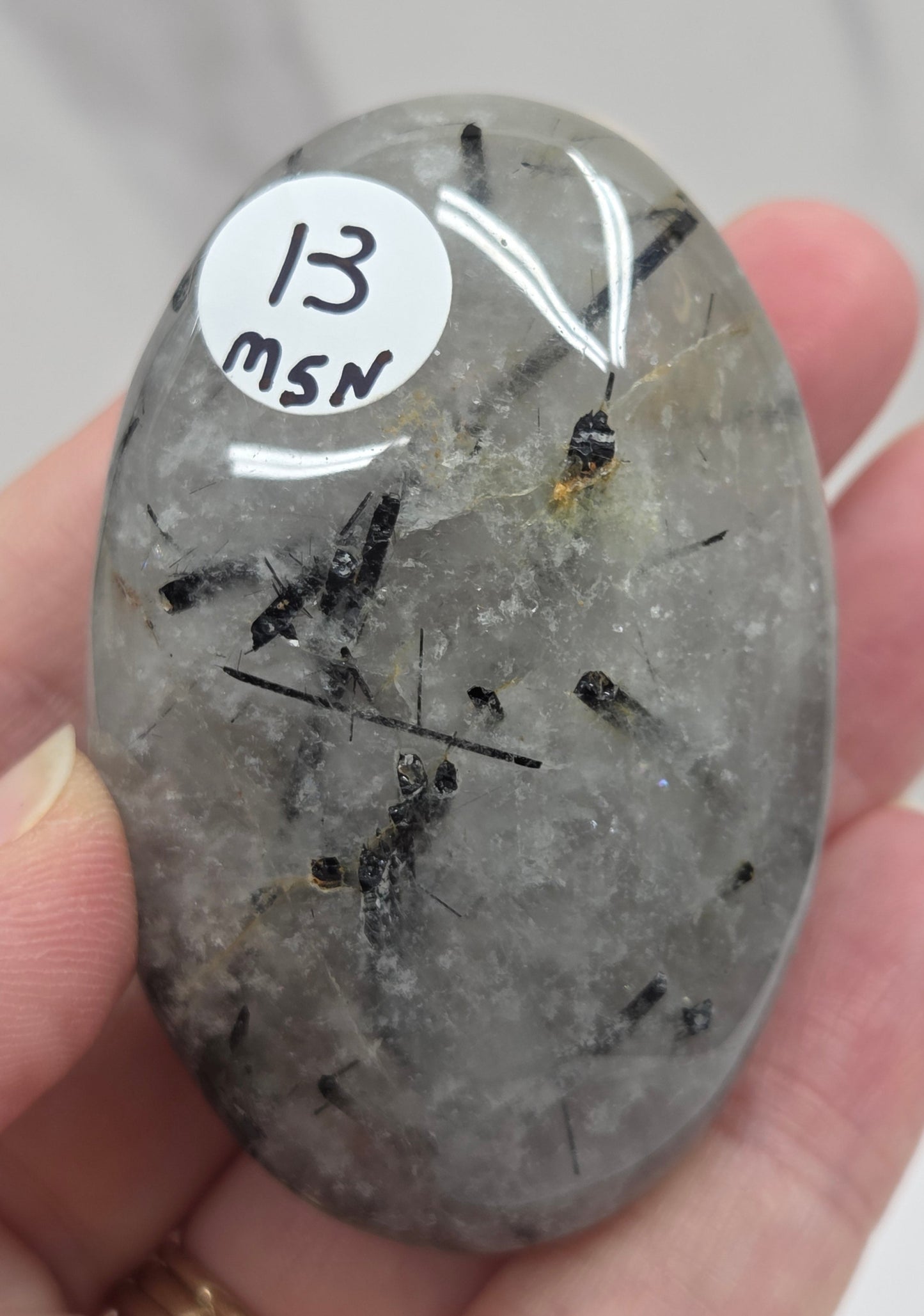 Palm shaped carving made of Quartz with Tourmaline inclusions being held in a hand on a white background