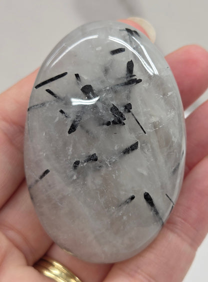 Palm shaped carving made of Quartz with Tourmaline inclusions being held in a hand on a white background