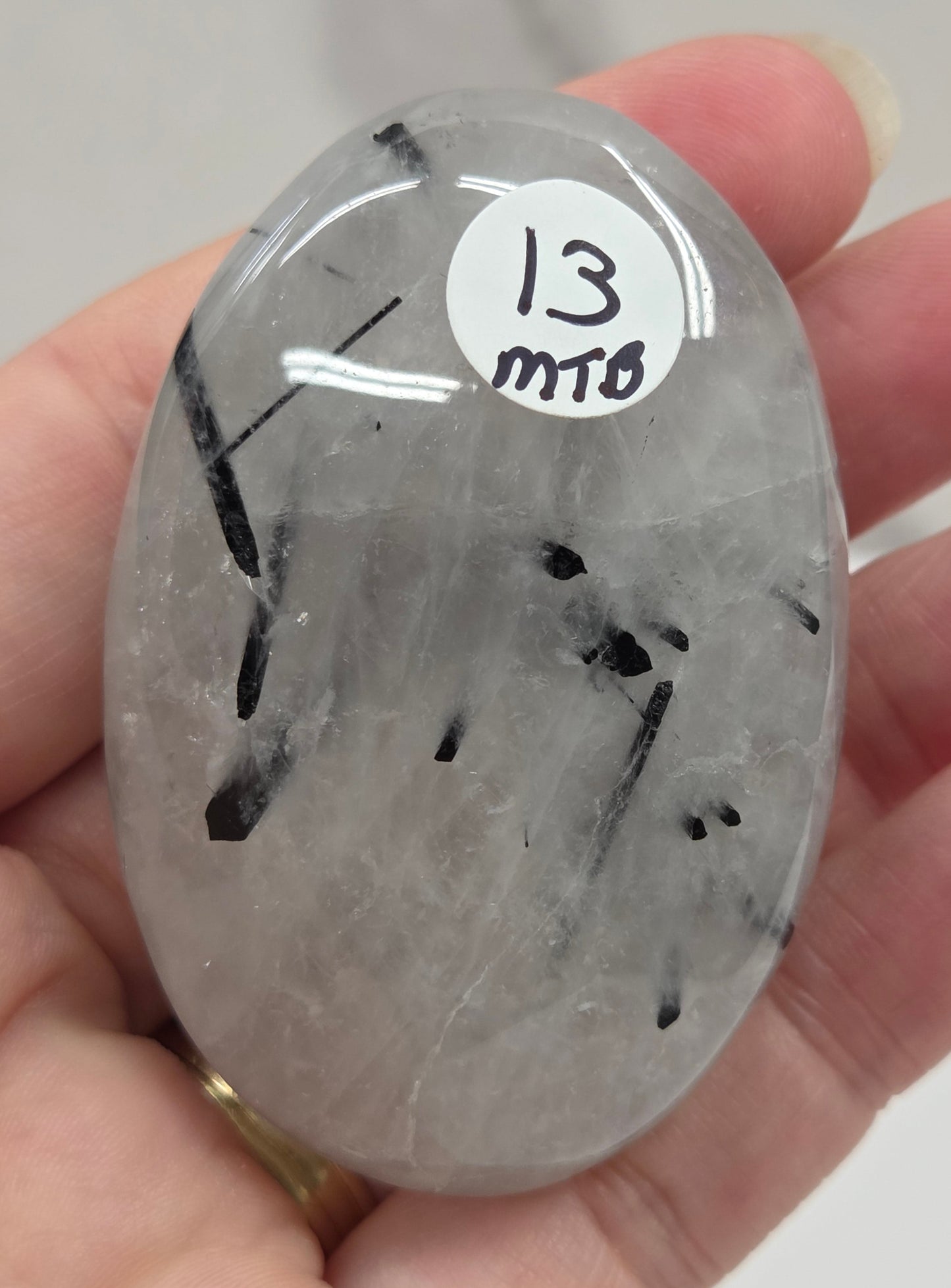 Palm shaped carving made of Quartz with Tourmaline inclusions being held in a hand on a white background