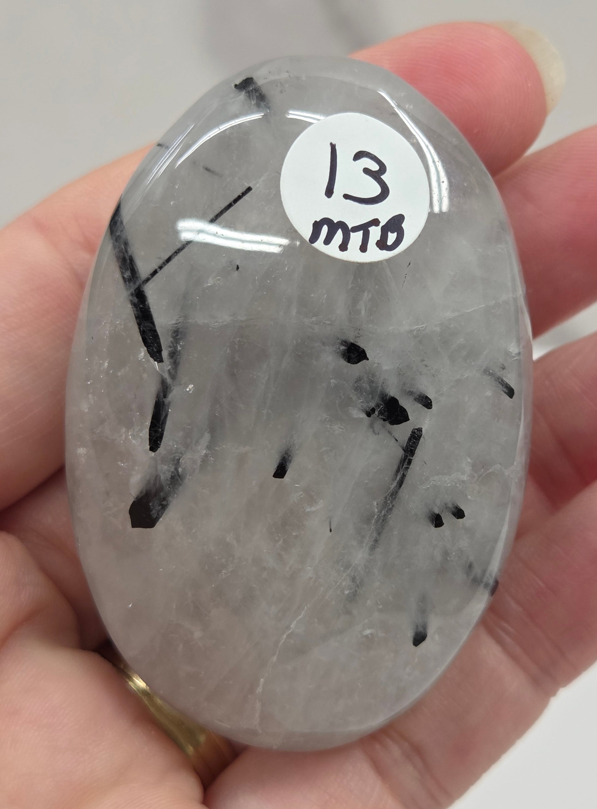 Palm shaped carving made of Quartz with Tourmaline inclusions being held in a hand on a white background