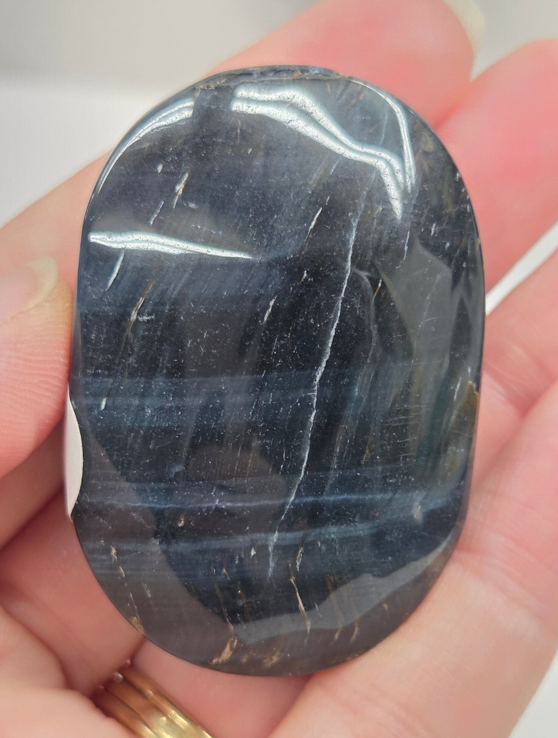 Blue Tiger's Eye palm carving being held in a hand against a white background
