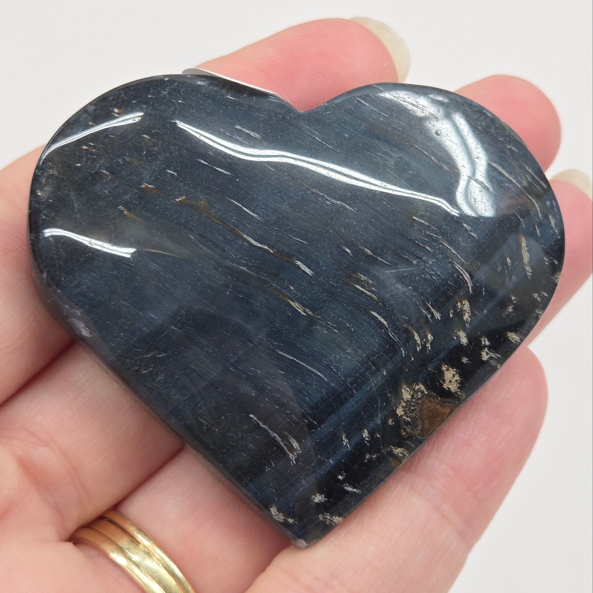 Blue Tiger's Eye heart carving being held in a hand against a white background