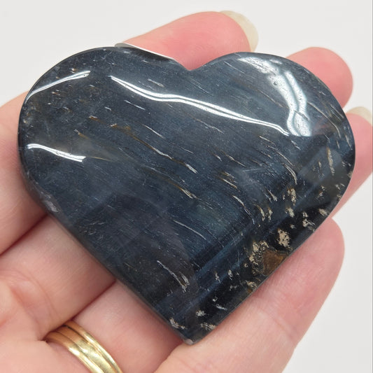 Blue Tiger's Eye heart carving being held in a hand against a white background
