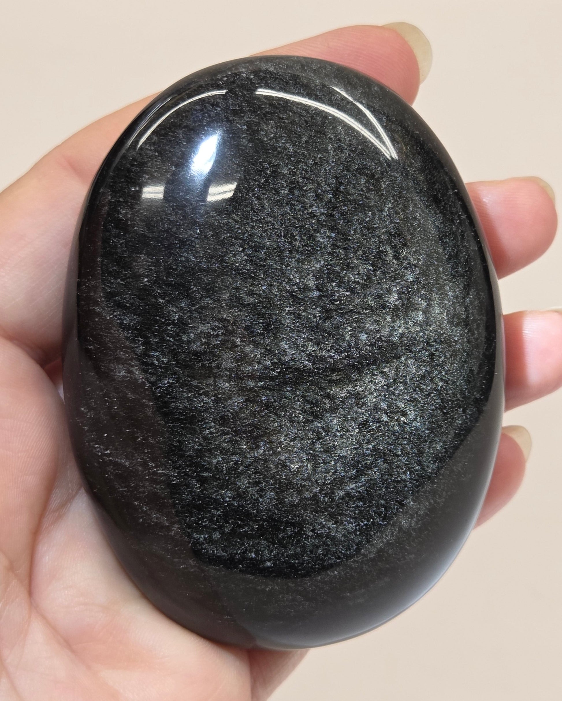 Silver sheen obsidian palm carving being held in a hand against a white background