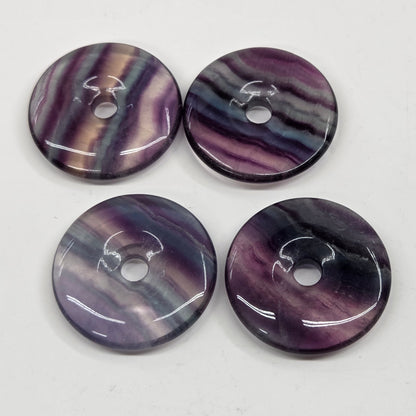 Multi-colored fluorite donut shaped carvings with banding on a white background