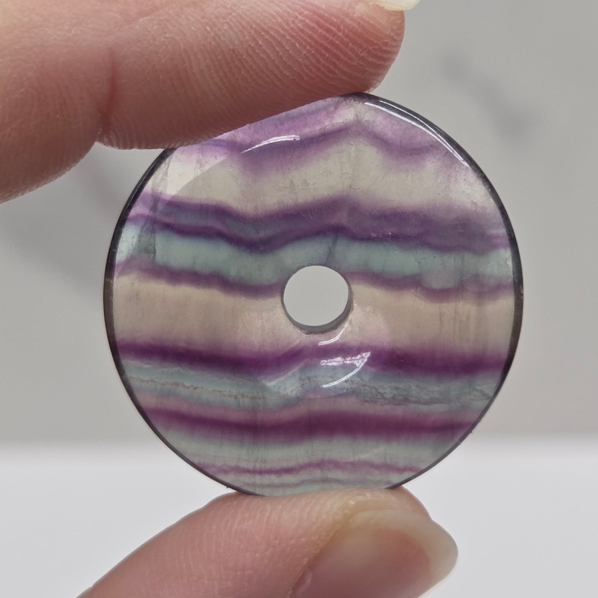 Hand holding a Multi-colored fluorite donut shaped carving with banding on a white background