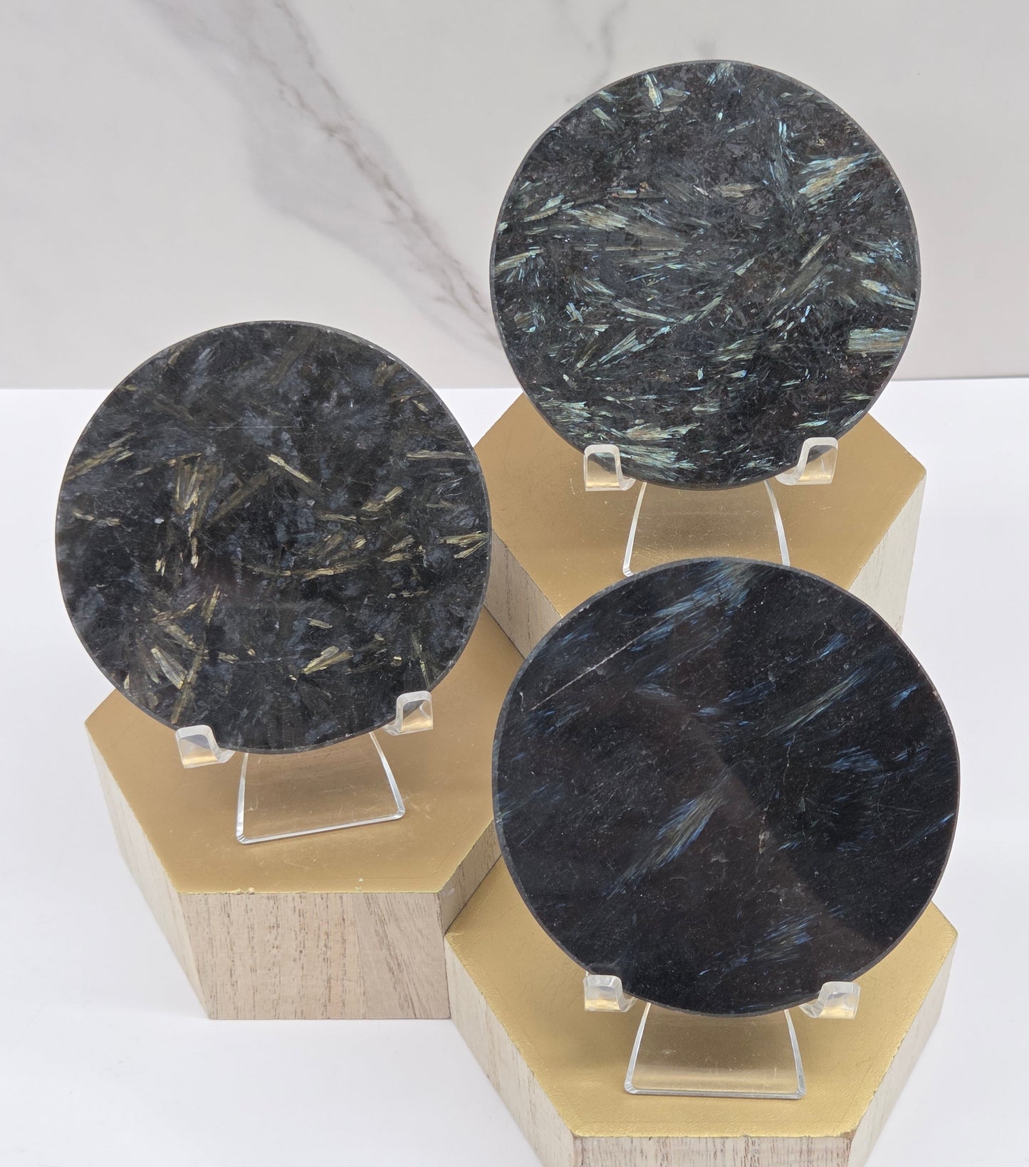 Astrophyllite round carvings with varying colors on acrylic stands on a wood stand against a white background