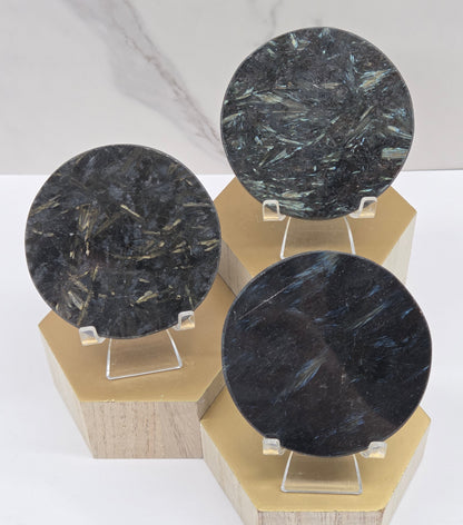 Astrophyllite round carvings with varying colors on acrylic stands on a wood stand against a white background