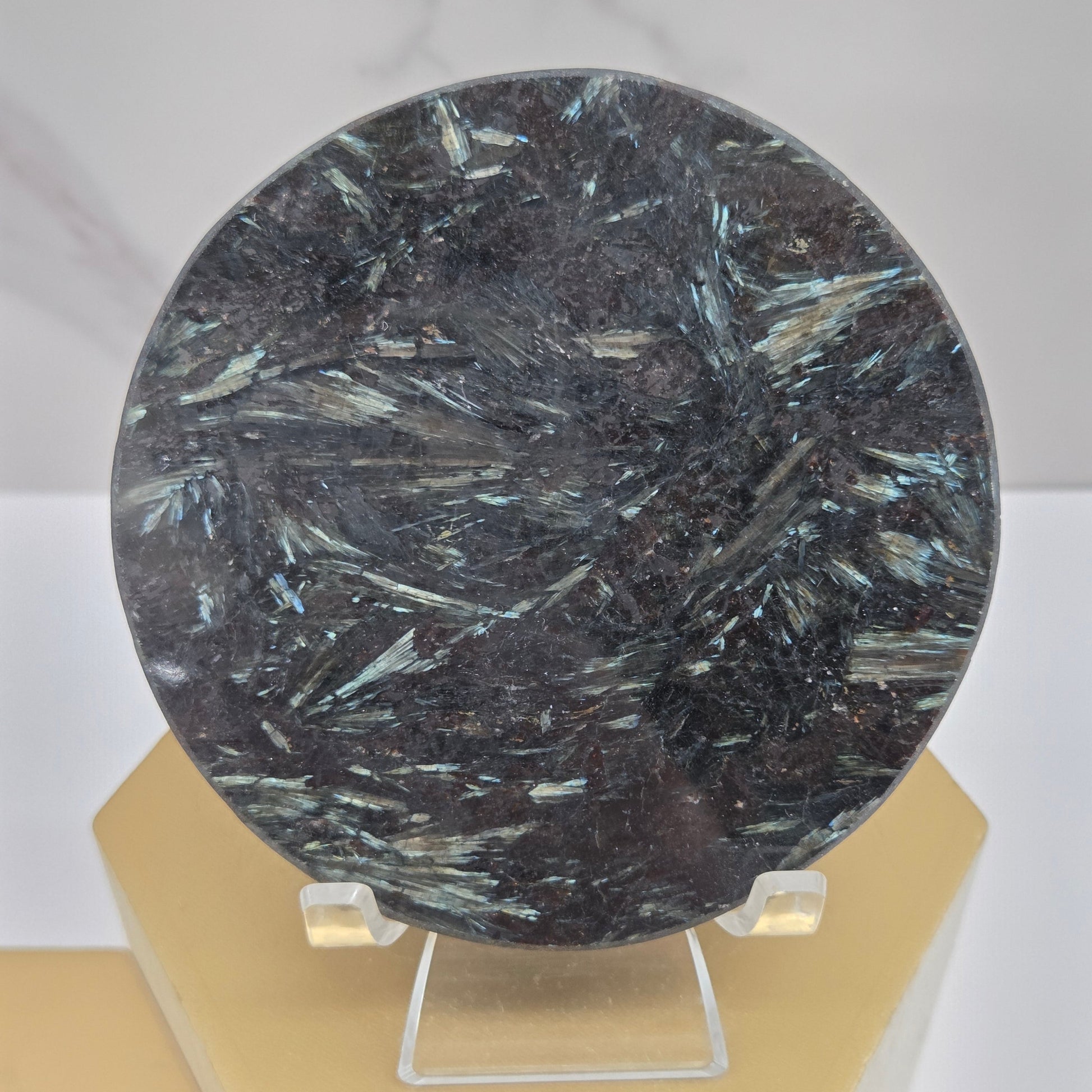 Astrophyllite round carving with varying colors on an acrylic stand on a wood stand against a white background