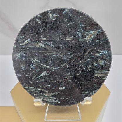 Astrophyllite round carving with varying colors on an acrylic stand on a wood stand against a white background