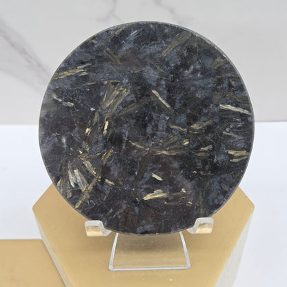 Astrophyllite round carving with varying colors on an acrylic stand on a wood stand against a white background