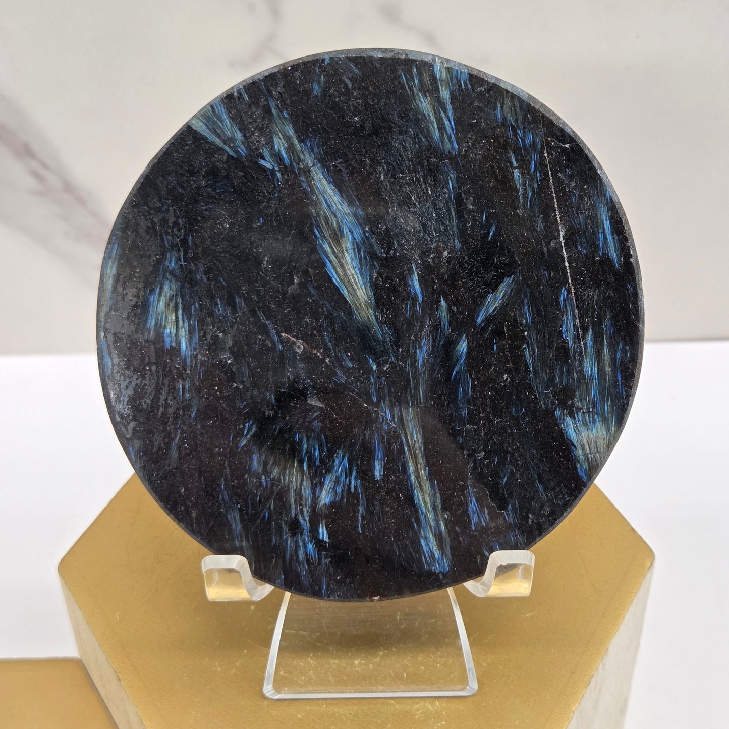 Astrophyllite round carving with varying colors on an acrylic stand on a wood stand against a white background