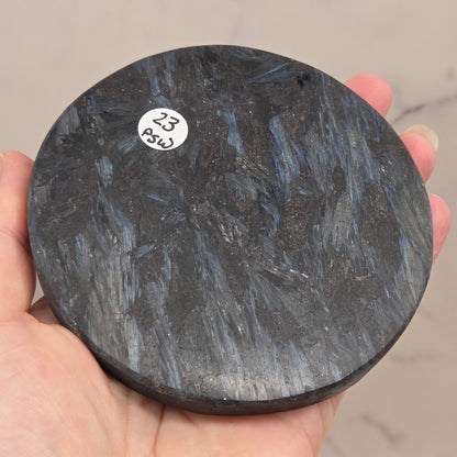 Astrophyllite round carving with varying colors on an acrylic stand on a wood stand against a white background