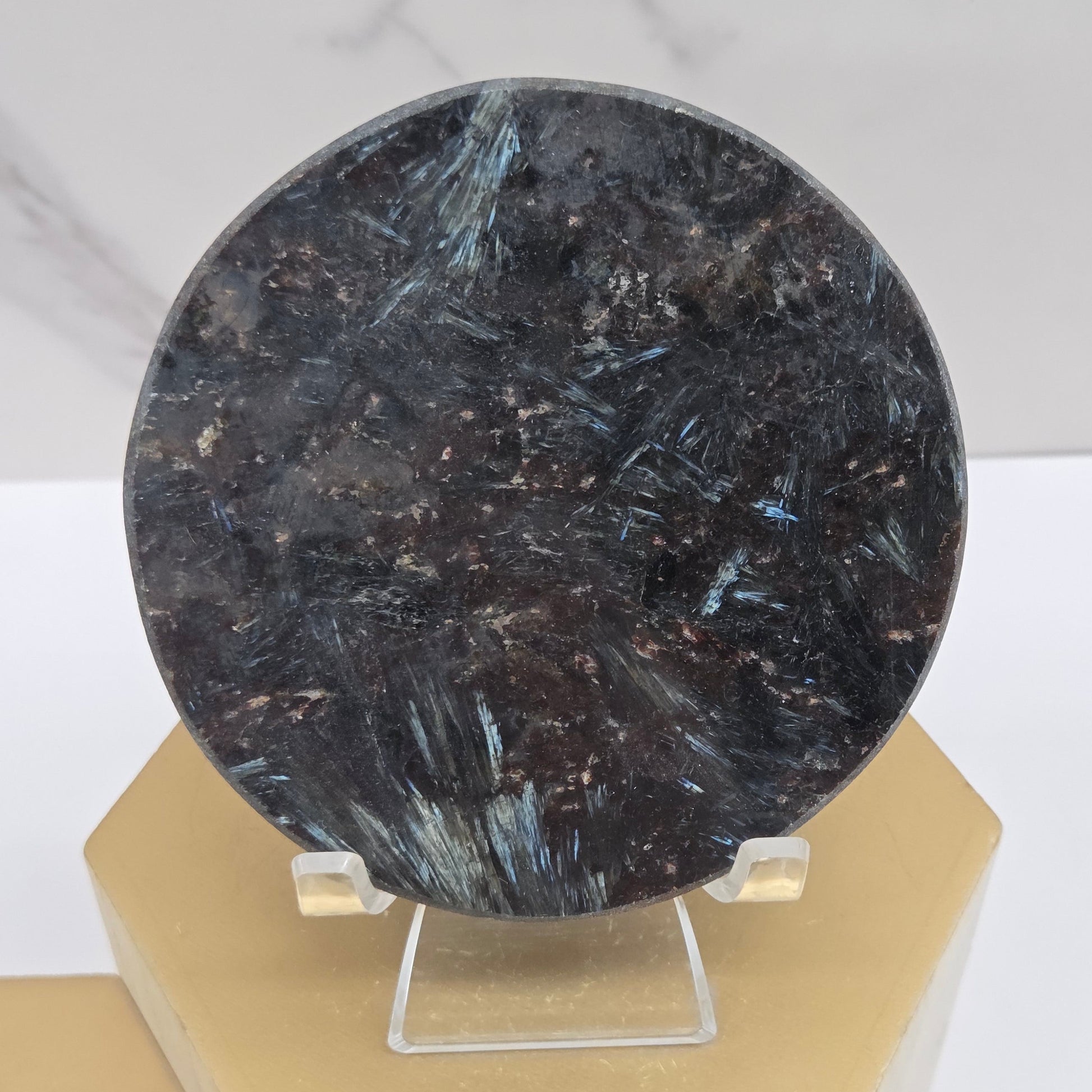 Astrophyllite round carving with varying colors on an acrylic stand on a wood stand against a white background